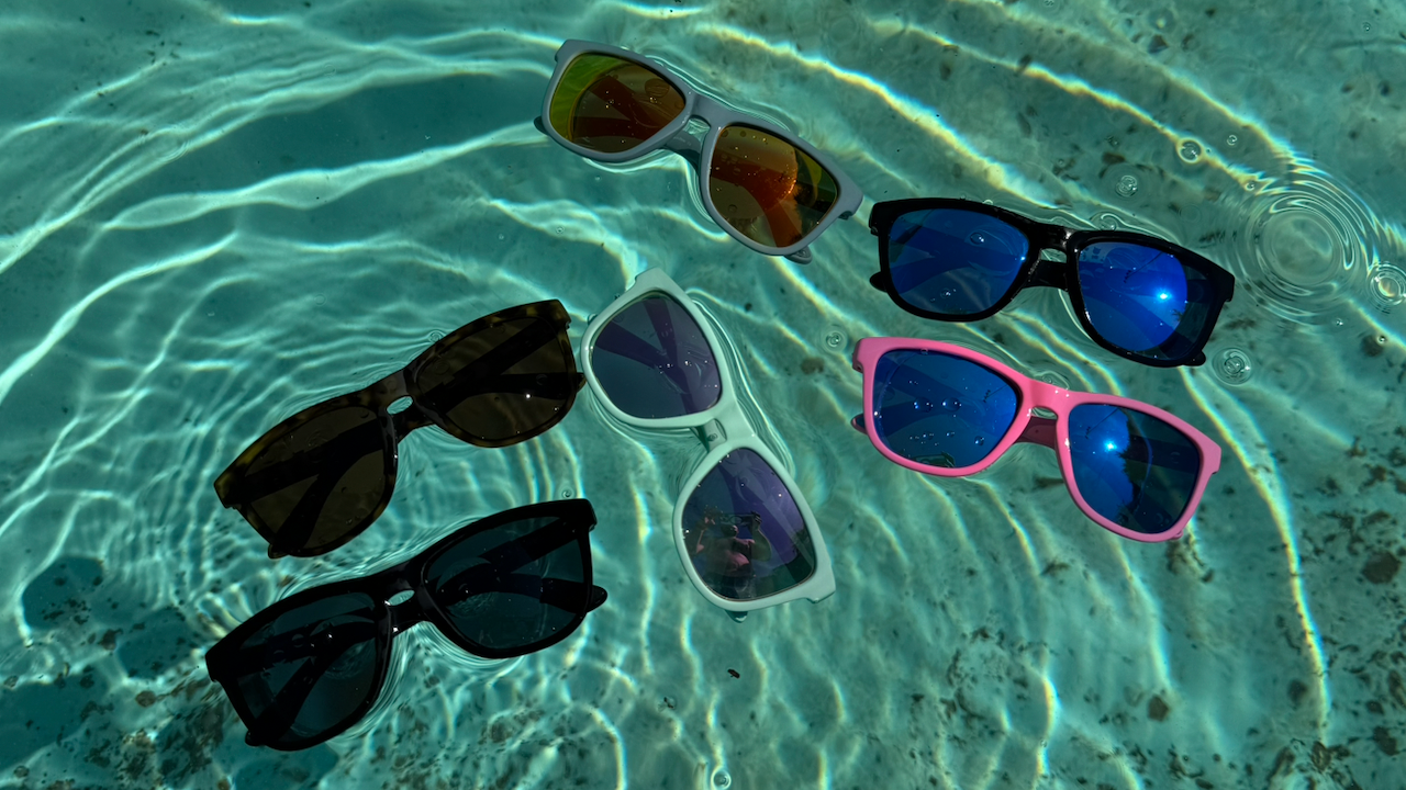 Five pairs of Floatys floating sunglasses on a clear blue water surface